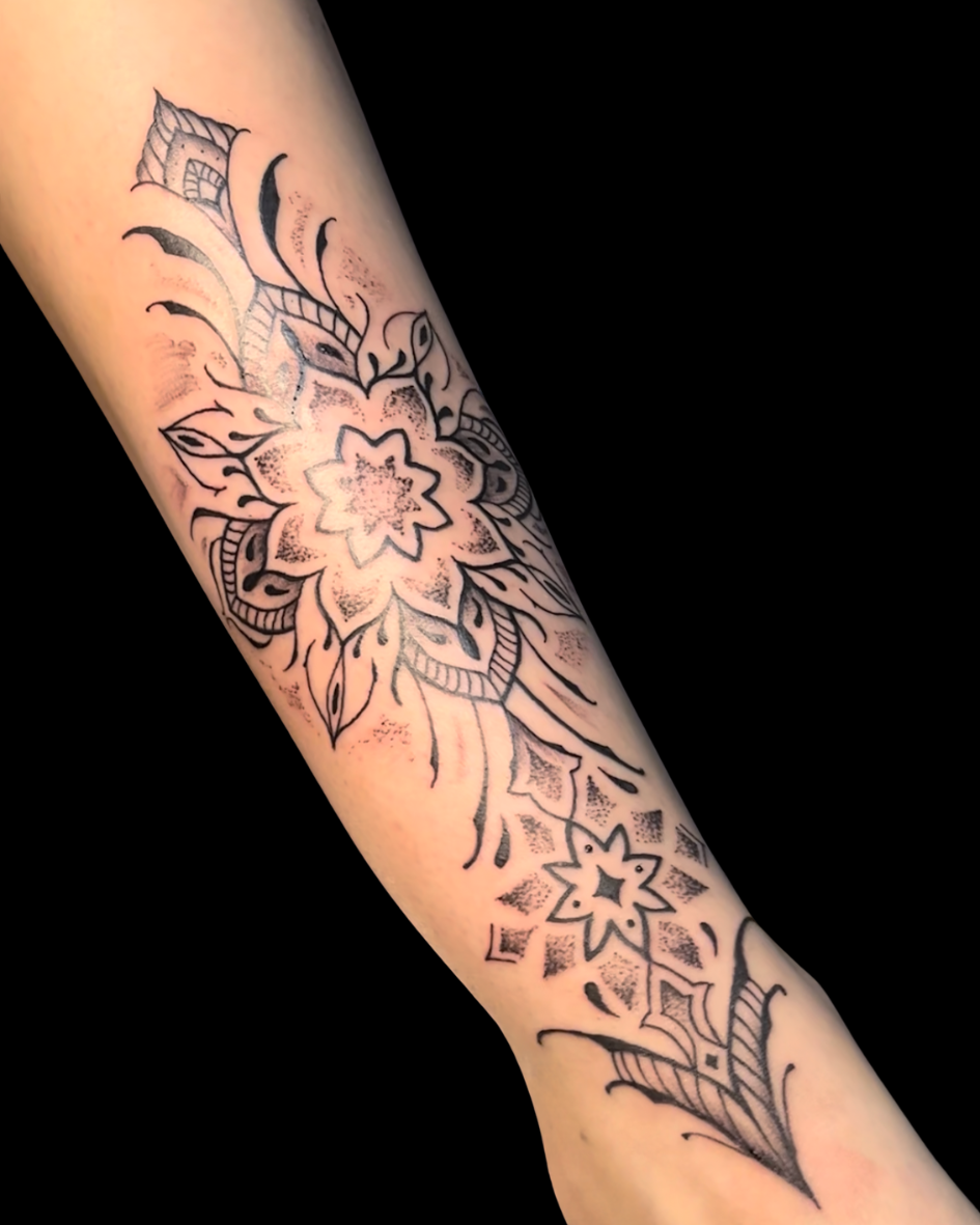 Tatuagem de mandala no antebraço em estilo ornamental. A arte floral e geométrica utiliza a técnica de pontilhismo (dotwork) e linhas finas para criar um design delicado que se estende pelo braço. Tattoo feminina e espiritual.