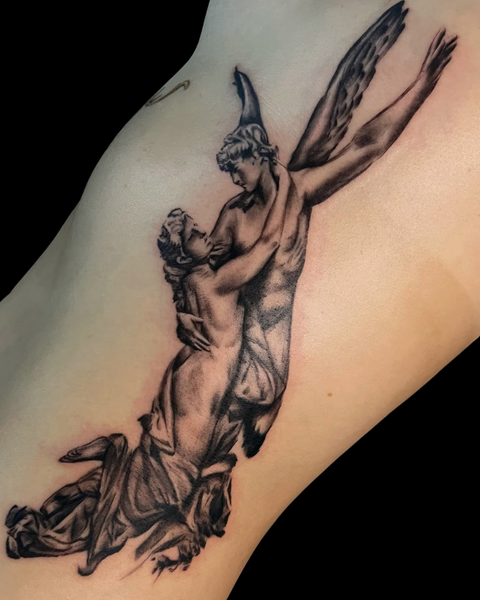 Tatuagem na costela baseada na escultura O Rapto de Psiquê de William-Adolphe Bouguereau. A arte em realismo preto e cinza retrata o deus Eros com suas asas, levantando Psiquê. Tattoo de mitologia grega com tema de amor e arte.