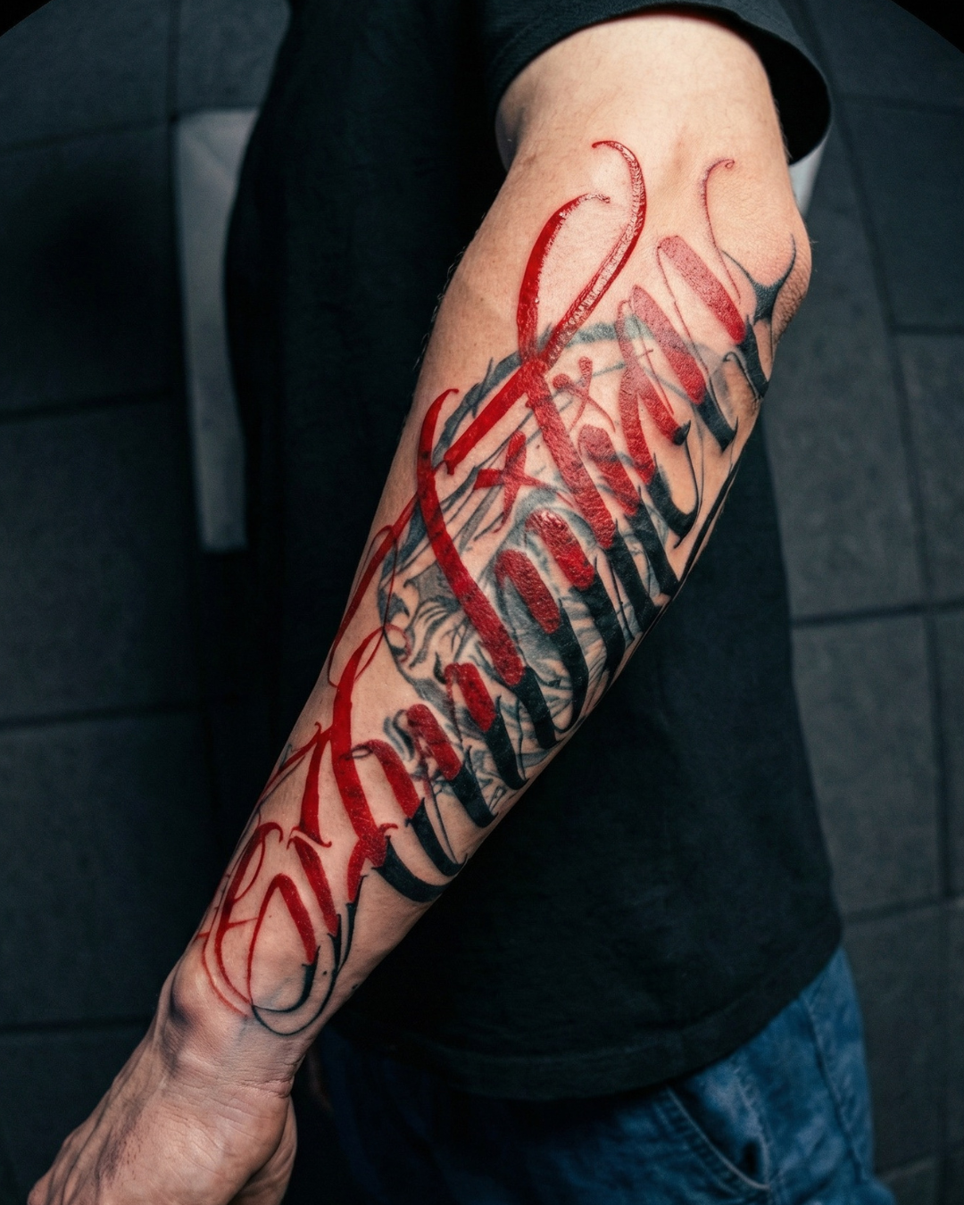Tatuagem personalizada de lettering no antebraço com traços caligráficos em preto e vermelho